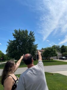 Woman and man standing close together and pointing at a blue sky with a few wispy clouds. 