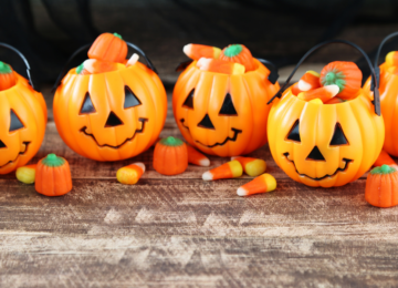 A row of pumpkin shaped Trick-or-Treat bags, filled with candy corn.