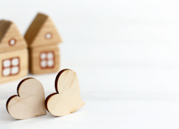Two decorative wooden hearts in front of two wooden decorative homes