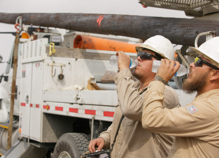 A photo of two AEP employees drinking water while working in the heat